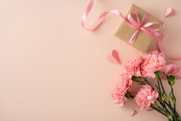 Fototapeta premium Happy Mother's Day concept featuring pink carnations, a wrapped gift with satin ribbon and paper hearts on a soft peach background ideal for cards and social media visuals