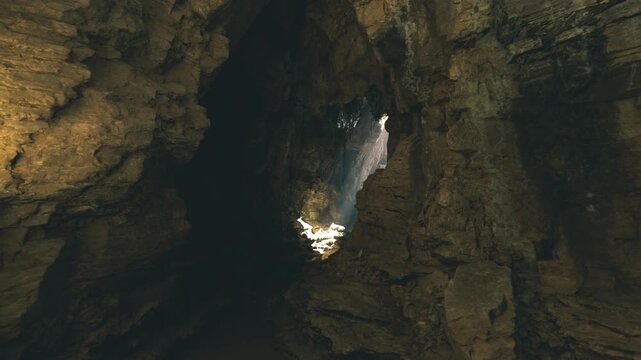 Hang son doong dramatic light shaft panorama displays tall cavern walls framing concentrated beam and illuminated vegetation patch, rich earth tones, strong