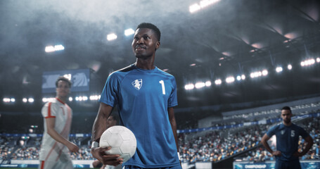 Black Male Soccer Captain Walks Across the Pitch Holding the Match Game Ball Before Kickoff, Leading His Side Into a Professional International Football Tournament in a Packed World Stadium. © Gorodenkoff