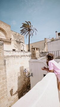 Woman enjoying a quiet moment on a sunlit terrace in southern Italy. Mediterranean architecture, palm tree, warm climate, slow living atmosphere, calm everyday life and peaceful southern lifestyle
