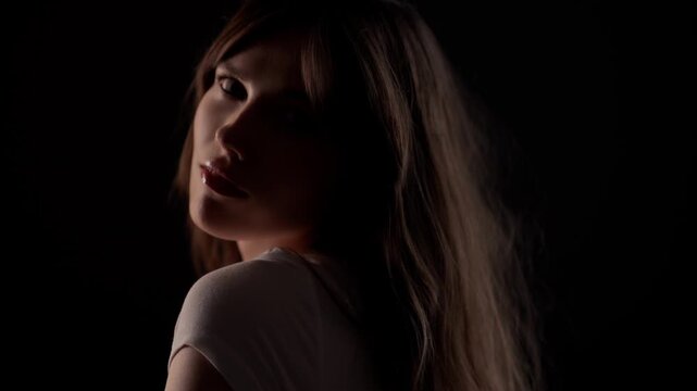 Vulnerability and emotional distress a woman looks back over her shoulder in the dark with cinematic lighting.