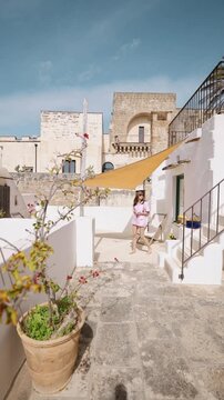 Static video of a woman stepping onto her terrace holding a cup of coffee in southern Italy. Mediterranean everyday life, warm morning light, calm routine and peaceful slow living atmosphere
