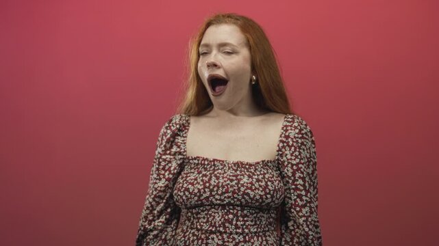 Redhead woman mouth open wide gasping, visible cleavage and square neckline, wearing floral dress in studio pink backdrop; surprise vulnerability.