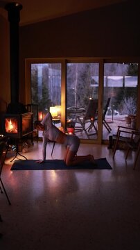Woman practicing gentle yoga near a fireplace in a cozy mountain house during winter. Warm candlelight, calm atmosphere, slow living lifestyle, evening relaxation indoors