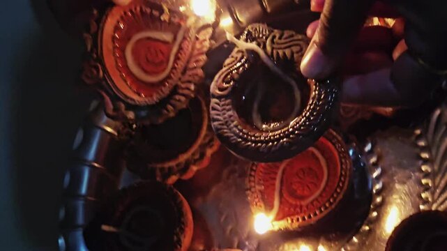 The woman lights one diya with another, using the burning wick Traditional clay oil lamps or diyas are commonly used in Hindu festivals such as Diwali to symbolize the victory of light over darkness.