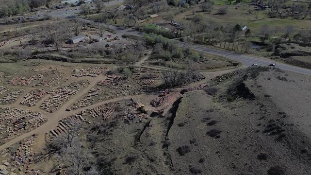 Industrial stone yard near CO 36 and Nelson Road with stacked materials, machinery, active work zones bordering open fields and nearby foothill slopes. Coarse surfaces, earthy tones, Longmont, CO