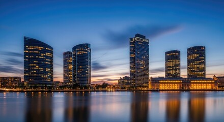 Naklejka premium City skyline at dusk modern architecture illuminated against a blue sky
