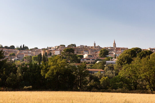 Vue panoramique sur le village proven&ccedil;ale perch&eacute; de La Cadi&egrave;re d&rsquo;Azur, arbres verts et champs de c&eacute;r&eacute;ales au premier plan, maisons de village et &eacute;glise sur la colline, ciel bleu, sud de la France