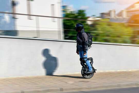 Man riding electric self balancing unicycle in urban environment wearing full protective gear and helmet during sunny day city commute. Micromobility scene, rider on electric unicycle EUC. Motion blur