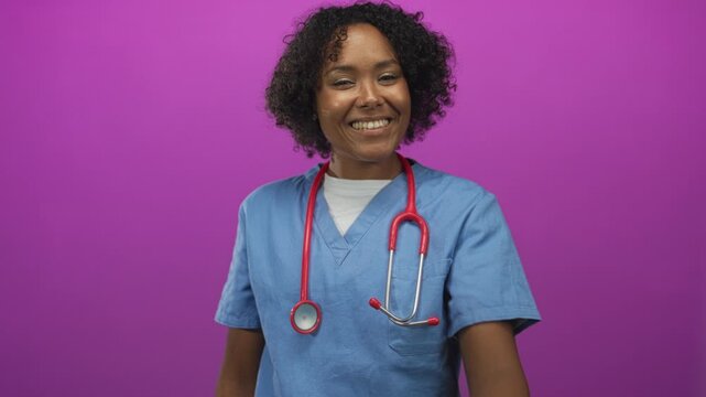 Young african american woman doctor in blue scrubs pinches her nose with one hand in a bright purple studio setting; disgust.