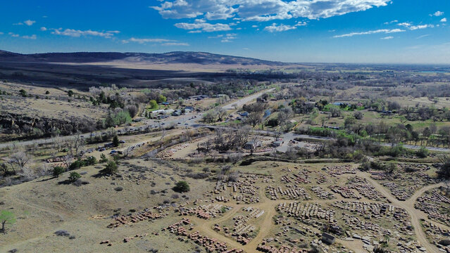 Stone yard foreground near N Foothills Hwy by Hygiene with organized slab rows leading toward nearby buildings and open land bordering foothill terrain. Rough surfaces, muted tones, Longmont, CO