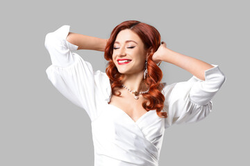 Fototapeta premium Beautiful young lady with red wavy hair on grey background