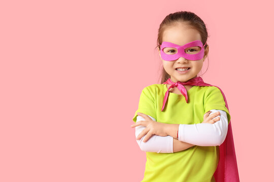 Cute little Asian girl in superhero costume on pink background