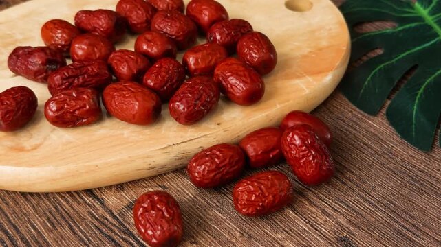 Dried red dates, known as jujubes, scattered on a natural wooden cutting board and warm rustic table, symbolizing ancient healthy superfood, traditional chinese medicine, and natural sweet snack