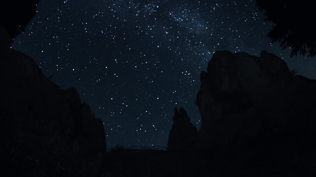 Night sky full of stars above dramatic rocky canyon with silhouettes of cliffs and trees. Silent Rocks of Tustan, Ukraine.