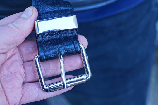 hand holding a black leather belt with a white metal buckle on a jacket