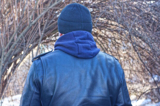 one man stands with his back in a black leather jacket and a hat on an autumn street