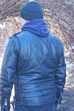 one man stands with his back in a black leather jacket and a hat on an autumn street