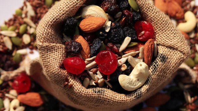 Mixed dried fruit filled in jute sack table top spin isolated on white background.