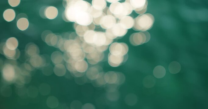 Sparkling sun highlights forming soft circular bokeh shapes on the calm emerald sea surface