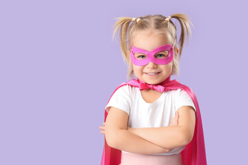 Fototapeta premium Cute little girl dressed as superhero on lilac background