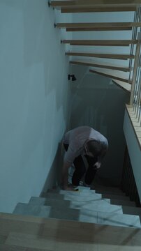 Vertical shot of a distracted man stumbling on a staircase after dropping his smartphone, showing everyday accident risk, loss of balance, and unsafe phone use at home.