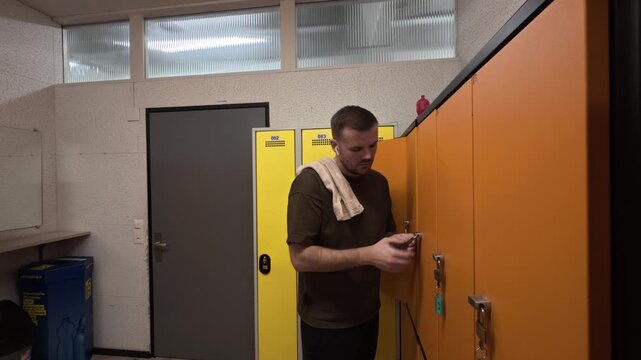Man in a gym locker room opening his locker with a key after training, showing post-workout routine, fitness lifestyle, and everyday changing room activity in a realistic sports setting.