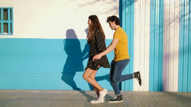 Two individuals of Hispanic descent dance energetically in an outdoor area. The bright colors of the surroundings enhance their joyful movements as they share laughs and make eye contact