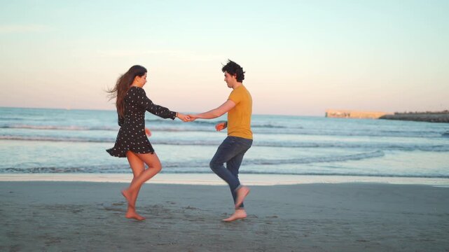 A Hispanic couple dances on the beach at sunset in Mexico. They laugh and enjoy the warm weather while moving together in the soft sand. The ocean waves add to the fun