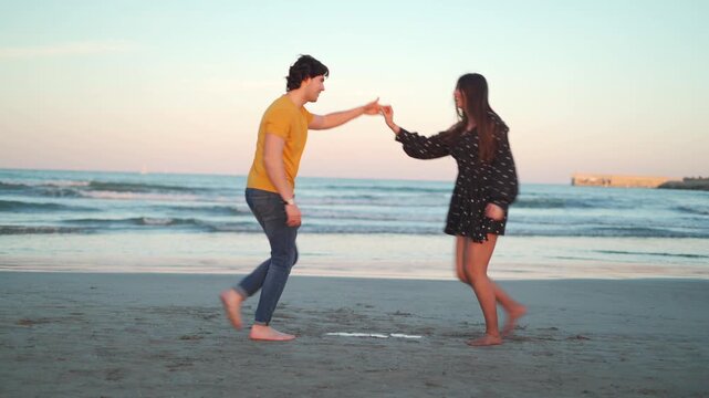 A man and woman of Hispanic ethnicity dance on the beach as the sun sets over the ocean. They hold hands and spin around, sharing smiles and laughter