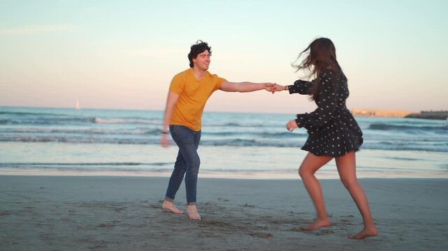A couple of mixed ethnicity dances happily on the beach at sunset. They enjoy the warm sand and the sound of waves while showcasing their dancing skills