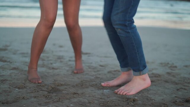 Two people enjoy dancing together on the sand as the sun sets over the ocean. Their bare feet touch the warm ground. They laugh and move freely in the moment