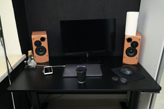 Modern black desk setup with computer monitor, speakers, and coffee cup