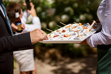 Close-up of a waiter serving appetizers on a tray during an outdoor business event or corporate reception