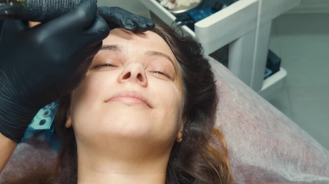 Technician applying microblading to a woman's eyebrows, creating natural looking hairstrokes for permanent makeup, enhancing beauty and facial features through cosmetic tattooing procedure
