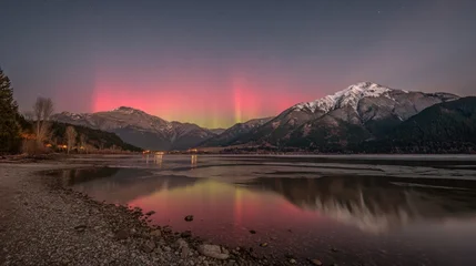 Poster Reflectie Vibrant Aurora Borealis glowing in pink and green hues above snow-capped mountains reflected in a serene lake at twilight.  © Lo