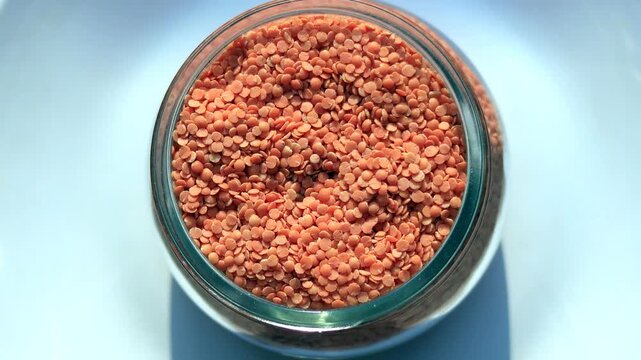 Red Lentil/ masoor dal filled in glass container table top spin isolated on white background.