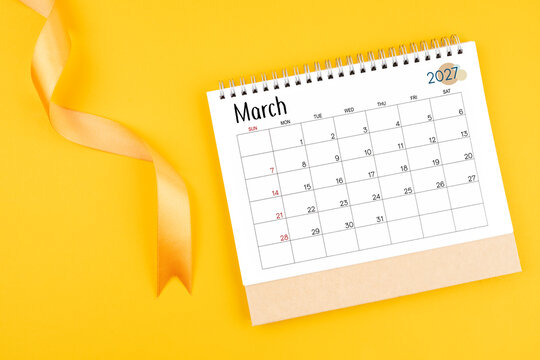 March 2027 desk calendar with yellow ribbon on yellow color background.
