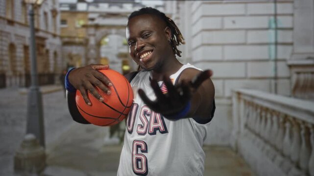 Man holding basketball with hand on ball wearing usa jersey on street, hand extended toward camera and smiling; team pride.