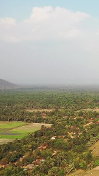 Drone shot of green rural landscape with scattered houses and fields near Banteay Samre, Cambodia. Expansive tropical vegetation under a partly cloudy sky.