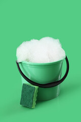 Fototapeta premium Plastic bucket with foam and sponge on green background
