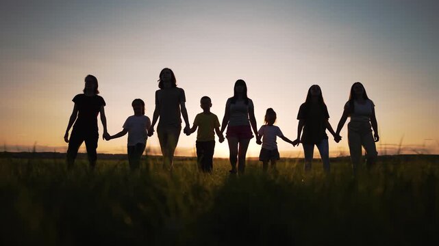 Holding hand together at sunset family and child silhouette in grassy field with woman and man linked in unity people walking across tall grass warm sky and calm horizon evoke connection unity
