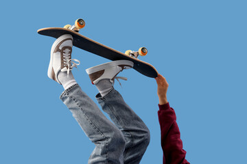 Legs of young man with skateboard on blue background, closeup © Pixel-Shot