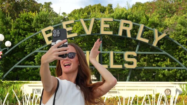 Stylish traveler taking a selfie by Beverly Hills sign in a sunny park