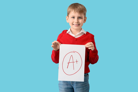 Happy schoolboy holding paper with a-plus grade on blue background