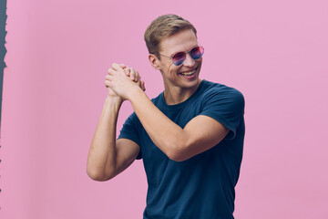 Fototapeta premium Happy smiling young man with sunglasses wearing casual blue t-shirt pose against pink background, cheerful cheerful expression, casual style, lifestyle concept, portrait photography, bright colors