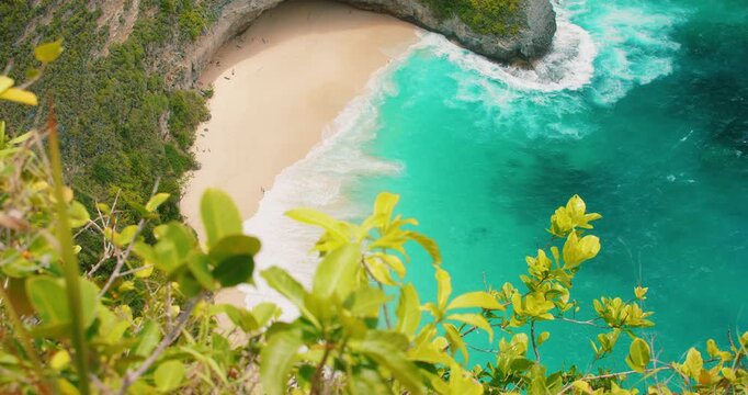 Ocean waves reach the white sand of Kelingking Beach below a green cliff in Nusa Penida