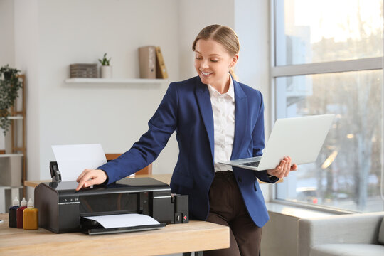 Young businesswoman with laptop using printer in office