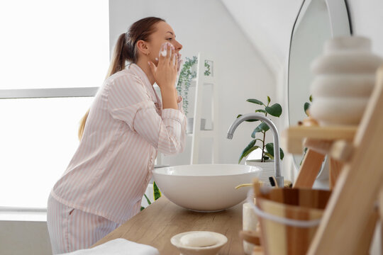 Young woman with soap washing her face near mirror in bathroom