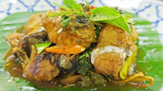 Authentic Thai Red Curry with Fish (Chu Chee Pla), garnished with coconut cream, fresh chili, and kaffir lime leaves on a banana leaf.